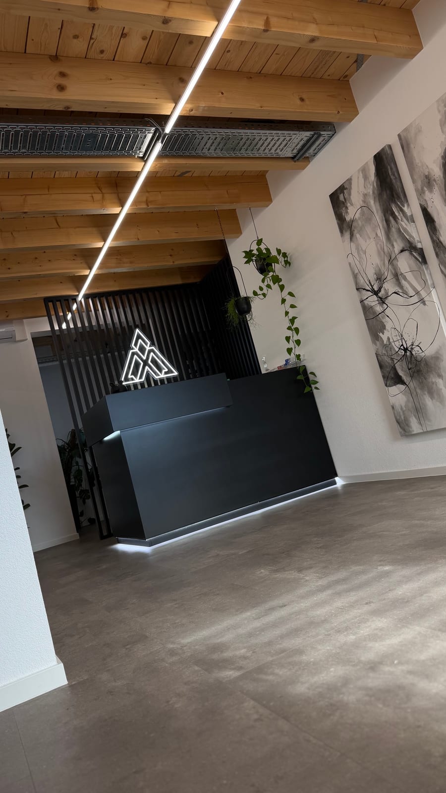 Schwarzer Empfangstresen mit Neon-Logo vor einer Lamellenwand, darüber Holzbalken